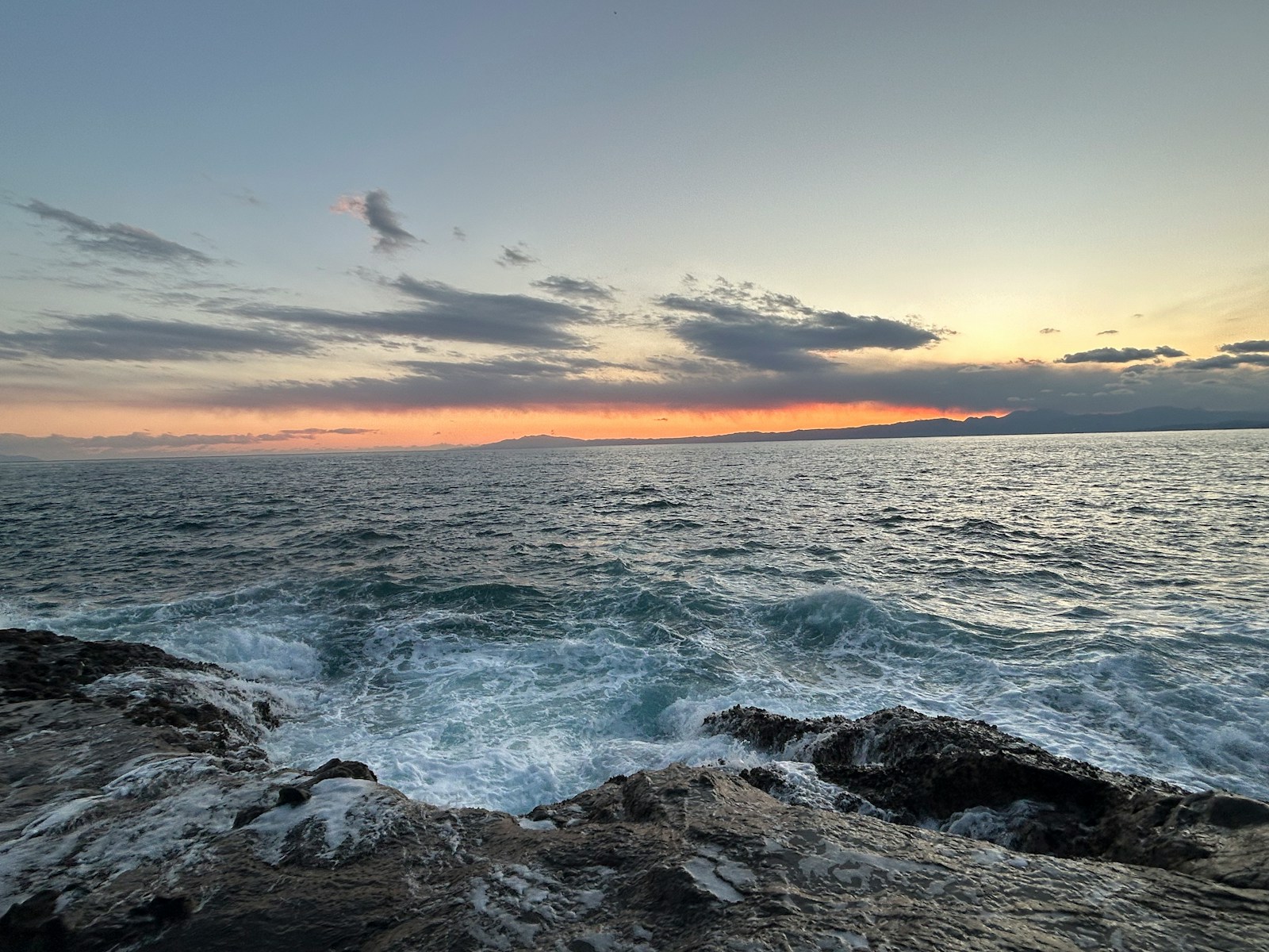 Sunset over ocean waves with rocky coast.